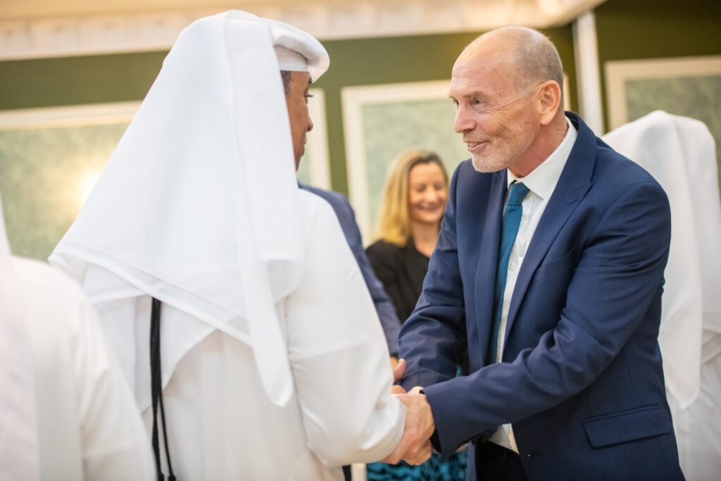 Two men, one British and one Qatari, shaking hands and smiling.