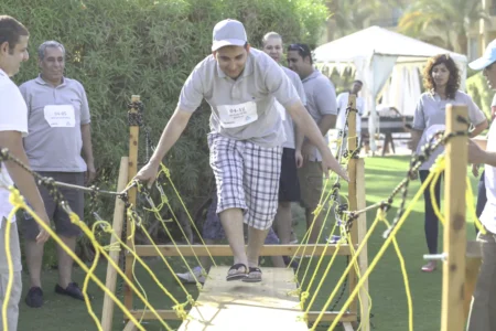 Man crossing a bridge built by his team, with the team cheering him on