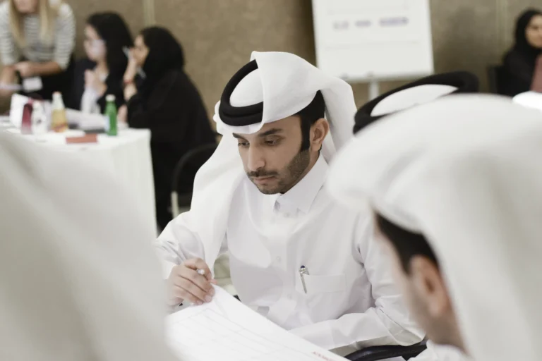 A Qatari man in a classroom, looking focused as he writes on a piece of paper.