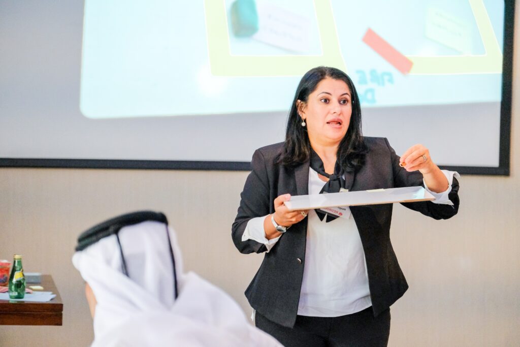 Woman standing in front of a whiteboard, passionately demonstrating an activity to a classroom.