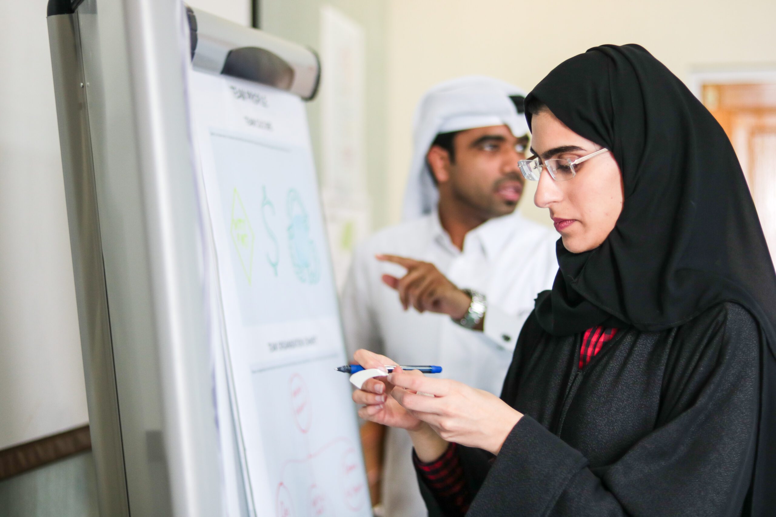 Woman looking at a piece of paper, standing in front of a whiteboard.