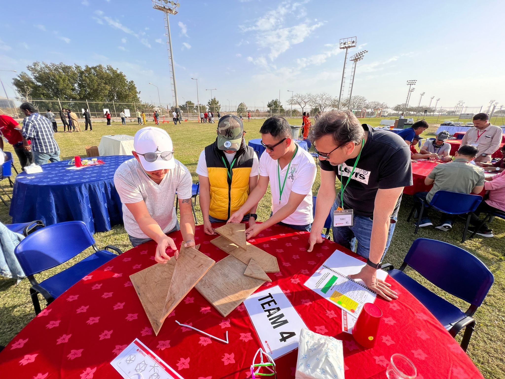 Four men trying to figure out a giant wooden puzzle while stood outside