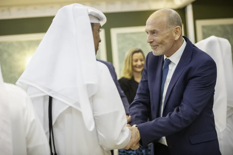 Two men, one British and one Qatari, shaking hands and smiling.